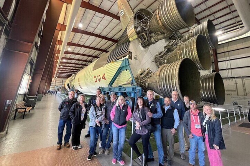 A group of people standing in front of a large rocket with multiple engines. 4