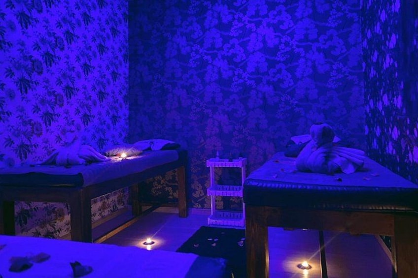Ett rum med två massagebänkar, där en person ligger på varje, och en liten hylla med ljus. 2