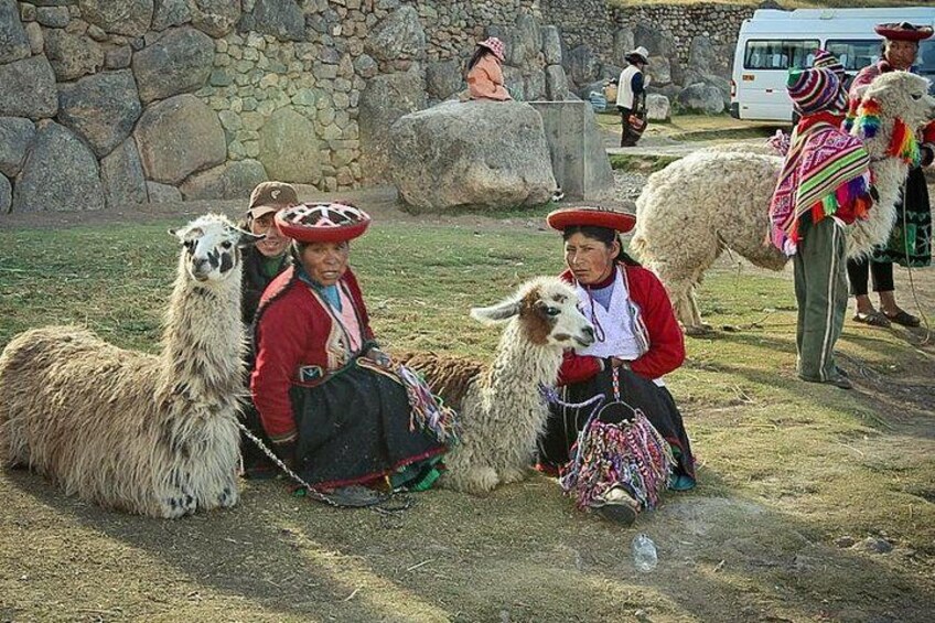 Des personnes, accompagnées de lamas et vêtues de costumes traditionnels, se trouvent dans un cadre rural, avec des murs de pierre et une construction en pierre en arrière-plan. 5