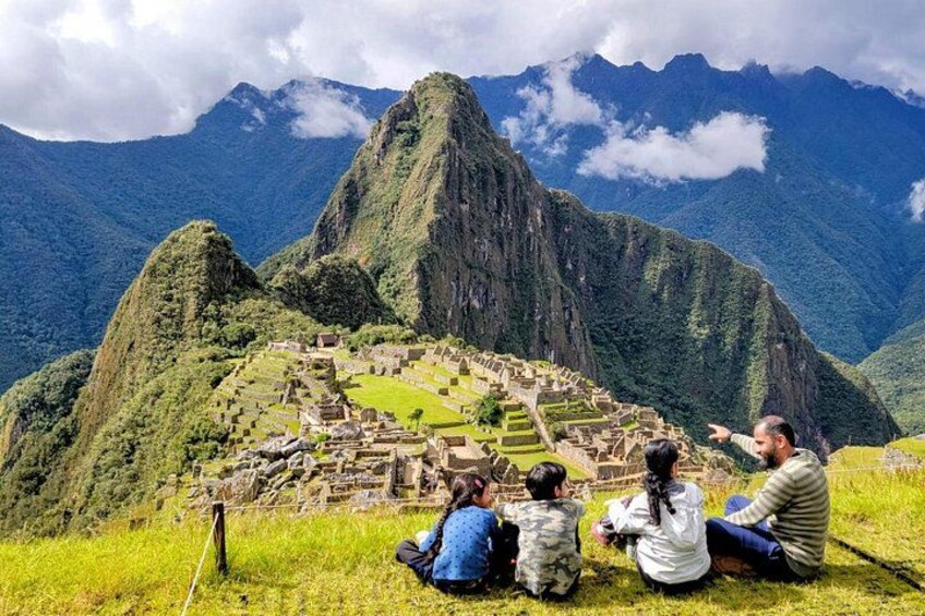 A group of people sitting on a grassy hill overlooking Machu Picchu. 1