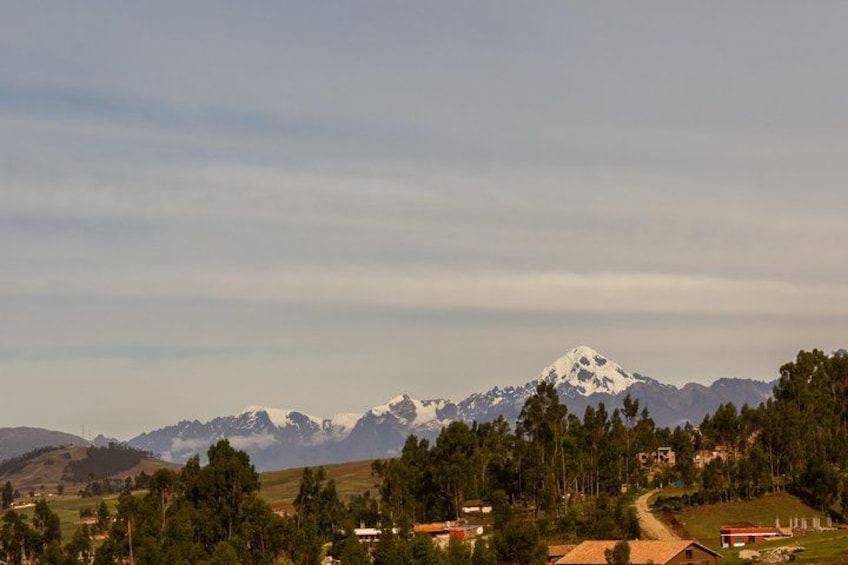A mountain range with snow-capped peaks, a forested valley, and scattered buildings. 3