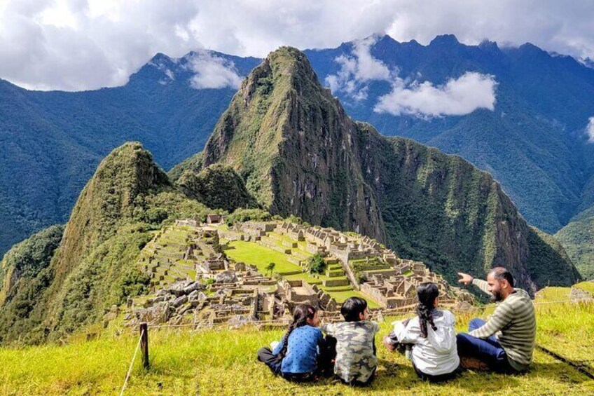 Machu Picchu ruïnes met toeristen die op een grashelling zitten. 1