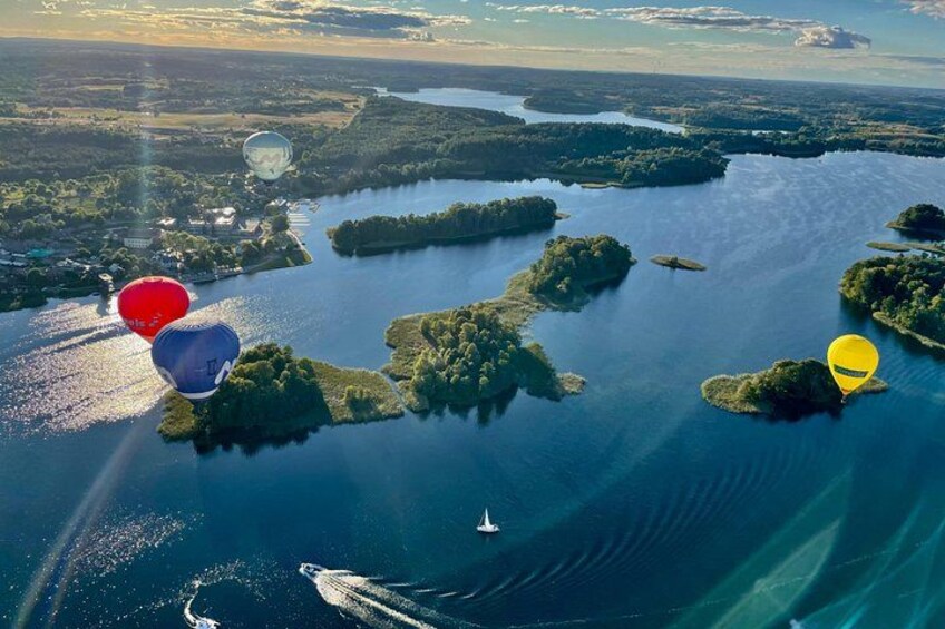 Vista aérea de un lago con varias islas, globos aerostáticos y un bote. 4