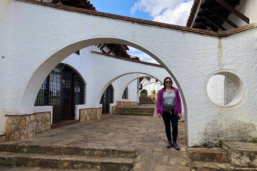 A person standing in a white-walled courtyard with arched doorways and a stone pathway. 2