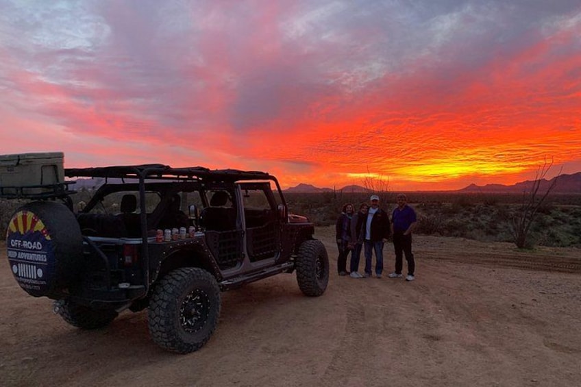 Un vehículo todoterreno negro estacionado en un camino de tierra con un atardecer al fondo. 4
