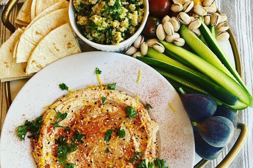 Une assiette de houmous garnie d’herbes et d’épices, accompagnée de pain pita, de concombres et d’un bol de salade. 2