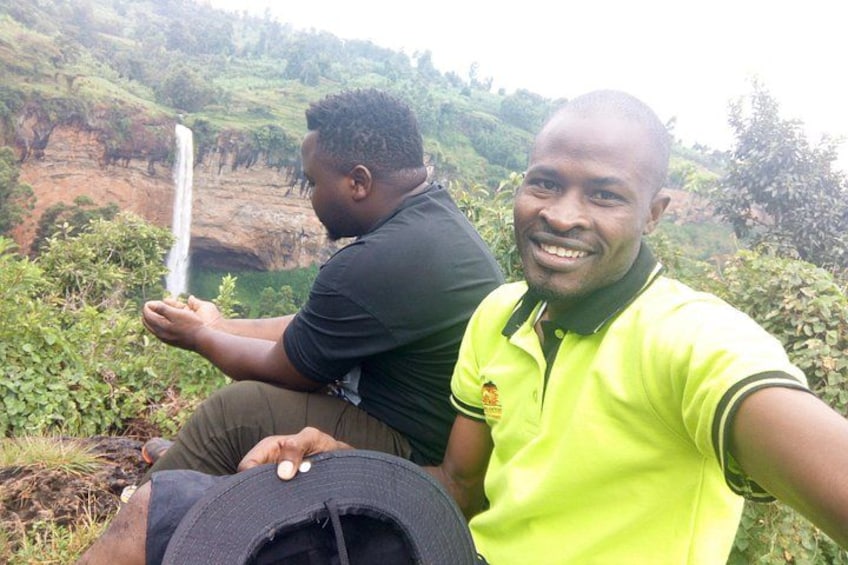 Two individuals sitting on a hillside with a waterfall in the background. 3