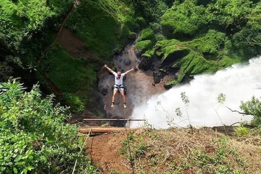 A person jumping off a cliff into a waterfall surrounded by lush greenery. 5