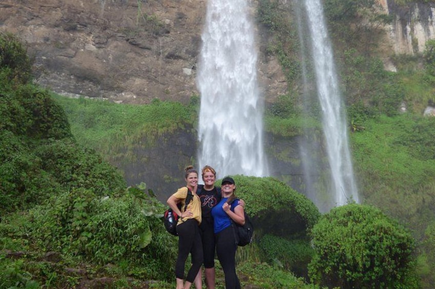 Three people standing in front of a waterfall with lush greenery around. 2