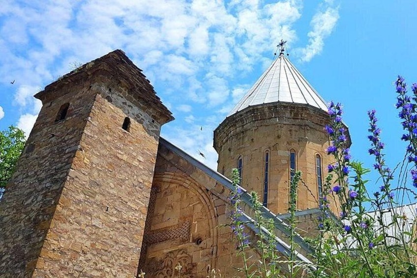 A stone tower and a round building with a conical roof, surrounded by vegetation. 1