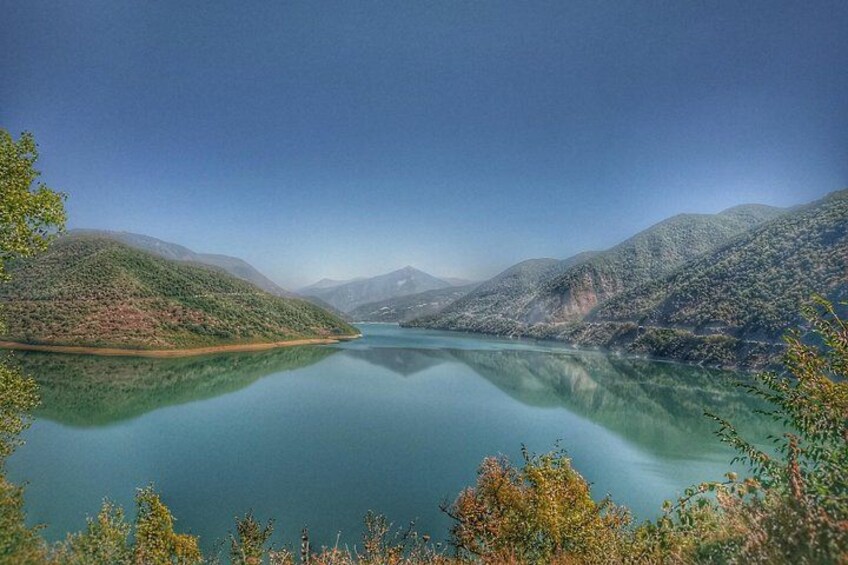 A calm lake surrounded by green hills and a clear sky. 4