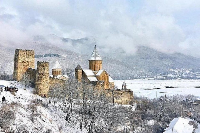 Un château de pierre historique, doté de nombreuses tours, entouré d’un paysage enneigé et avec des montagnes en arrière-plan. 1