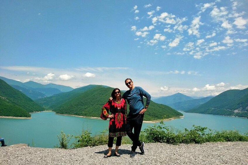 Two people standing on a gravel path overlooking a lake with mountains in the background. 2