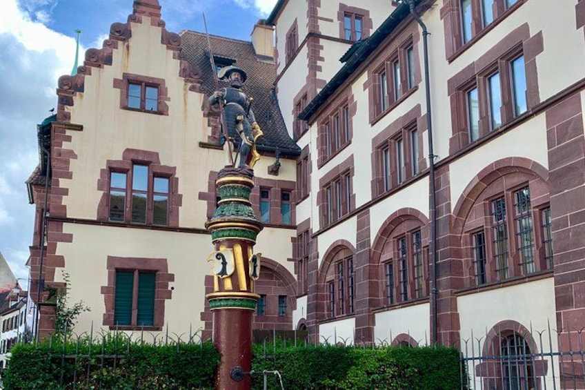 Un edificio histórico con una estatua sobre un pilar, rodeado de follaje. 4