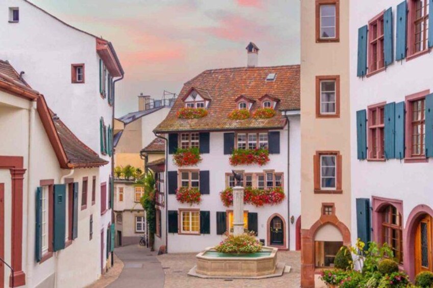 Una calle estrecha con edificios, una fuente y macetas con flores. 3