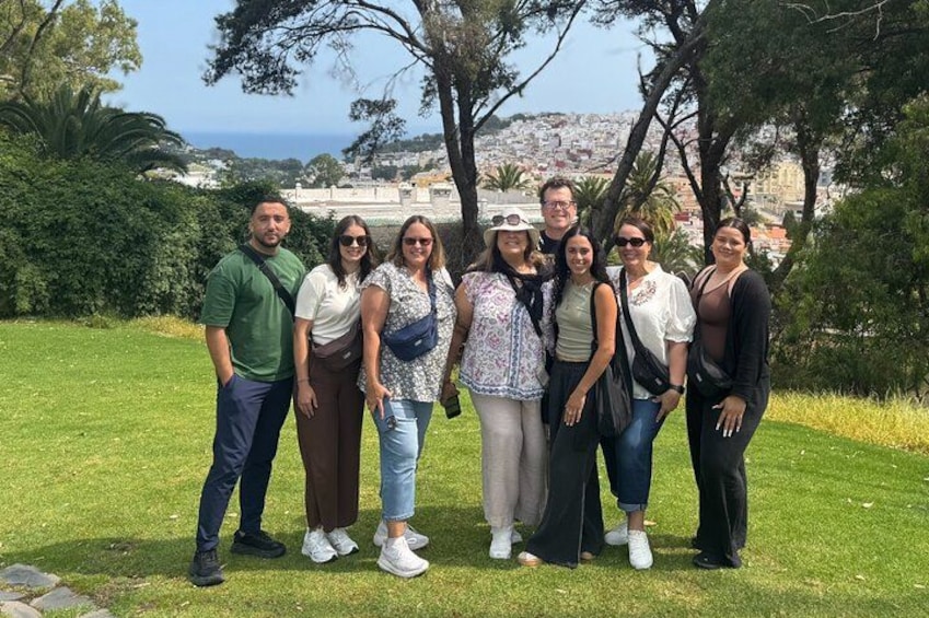 Un grupo de personas de pie sobre césped, con árboles y un paisaje urbano lejano al fondo. 1
