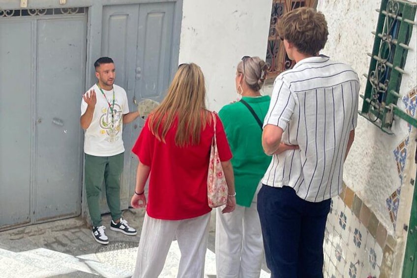 Un grupo de personas de pie en una calle estrecha con una puerta azul y una pared de azulejos. 5