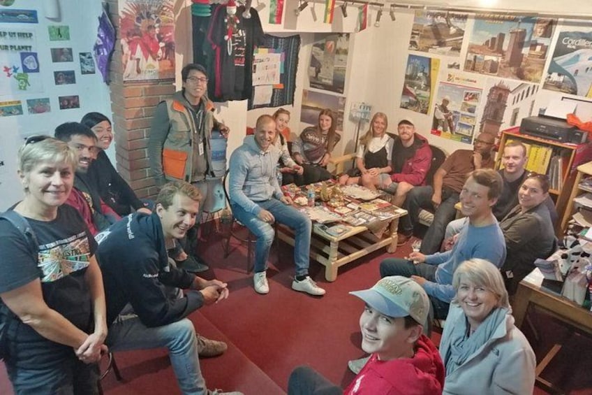 Een groep mensen zit rond een tafel in een ruimte met diverse posters en objecten aan de muren. 3