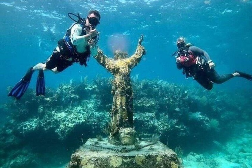 Two divers underwater near a submerged statue surrounded by marine life. 4