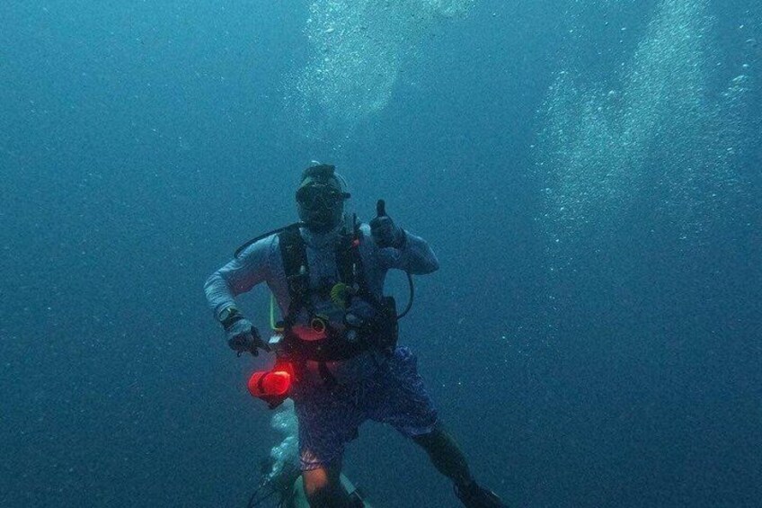 A diver in a blue wetsuit with a red light, underwater. 3
