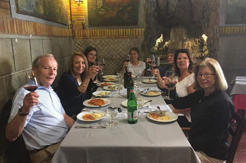 En gruppe mennesker spiser middag på en restaurant med en stenvæg og et maleri i baggrunden. 3