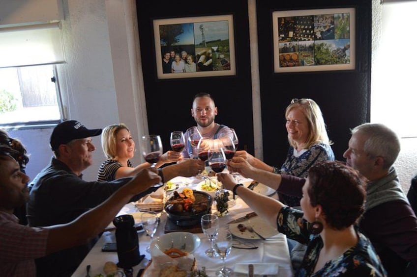 Un groupe de personnes porte un toast autour d’une table, des verres de vin à la main, le tout étant disposé sur une nappe blanche et entouré de différents plats. 4
