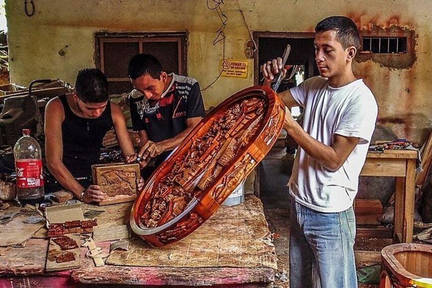 A workshop with three individuals working on a wooden object, possibly a musical instrument, with tools and materials scattered around. 5
