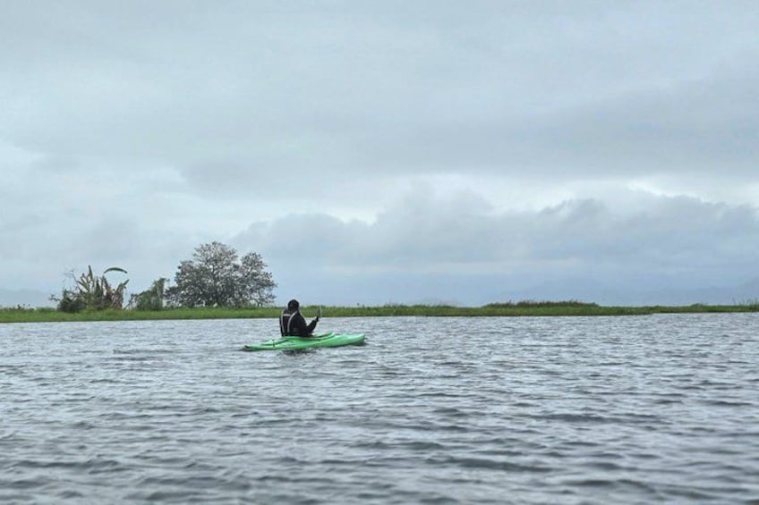 A person kayaking on a body of water with a cloudy sky and distant vegetation. 2