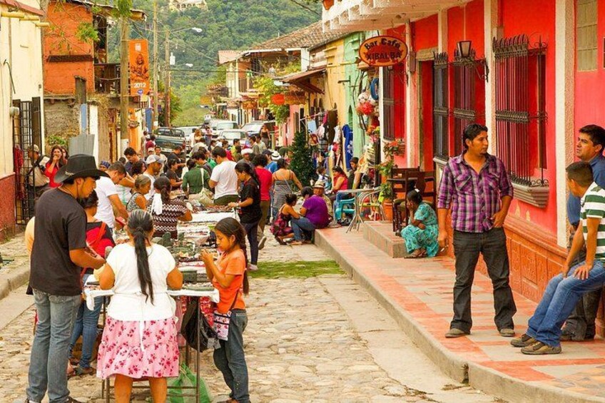 A bustling street scene with people gathered around tables, possibly for a market or social event. 2