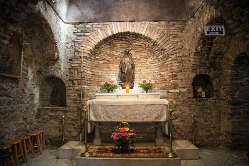 Une pièce aux murs de pierre, ornée d’une statue, d’une table avec des fleurs et d’un panneau indiquant la sortie. 3
