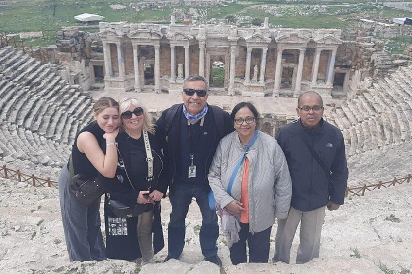 A group of people standing in front of an ancient amphitheater with stone seating and a central stage. 3