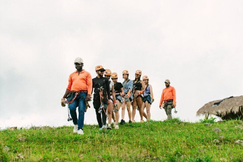 A group of people on a grassy hill with helmets, one person in an orange shirt leading. 3