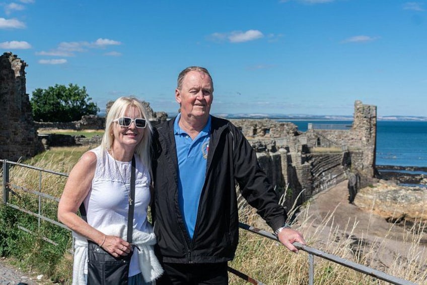 A couple standing by a historical site with ruins and a coastal view. 1
