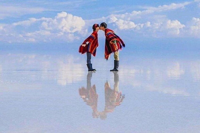 Deux personnes se tiennent sur une surface réfléchissante, avec un ciel dégagé et des nuages en arrière-plan. 2