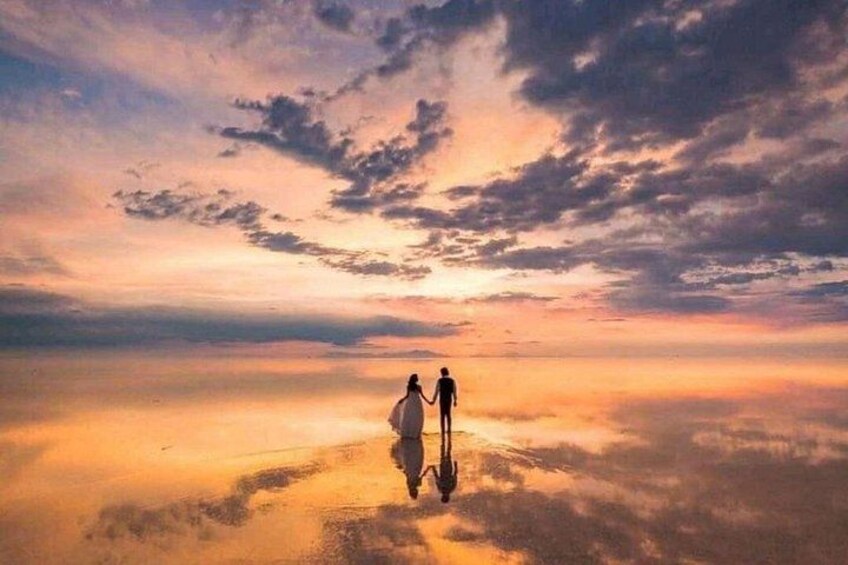 Deux personnes se tenant la main sur une surface réfléchissante, avec un ciel au coucher du soleil en arrière-plan. 3