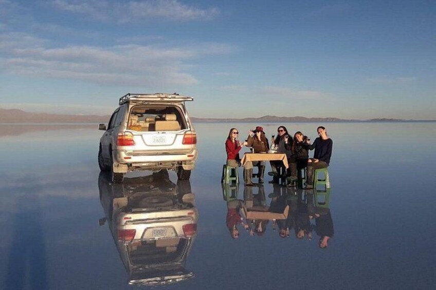 A group of people sitting on stools by a reflective surface, with a vehicle parked in the background. 5