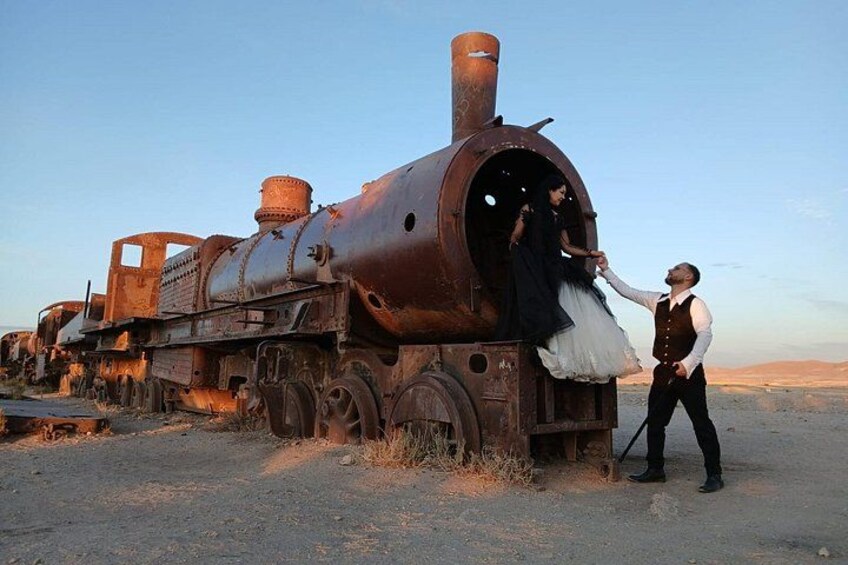 A rusted train engine with a person in a dress standing on the tracks. 1