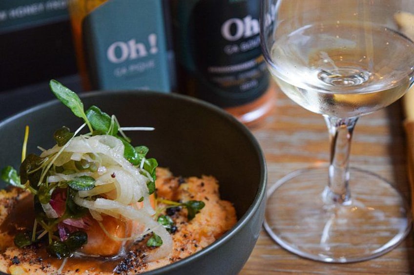 A bowl of food with a glass of white wine on a wooden table. 1