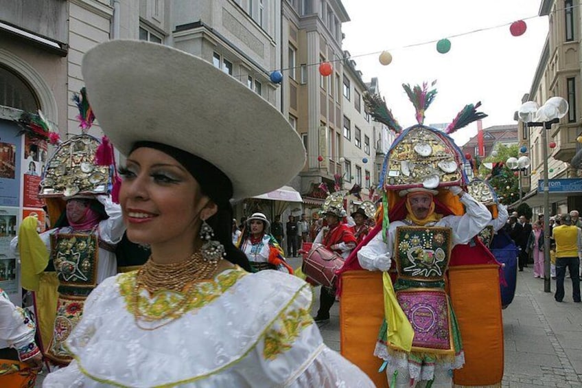 A person in a traditional costume with a large hat and a colorful outfit, walking on a street with buildings and other people in the background. 3