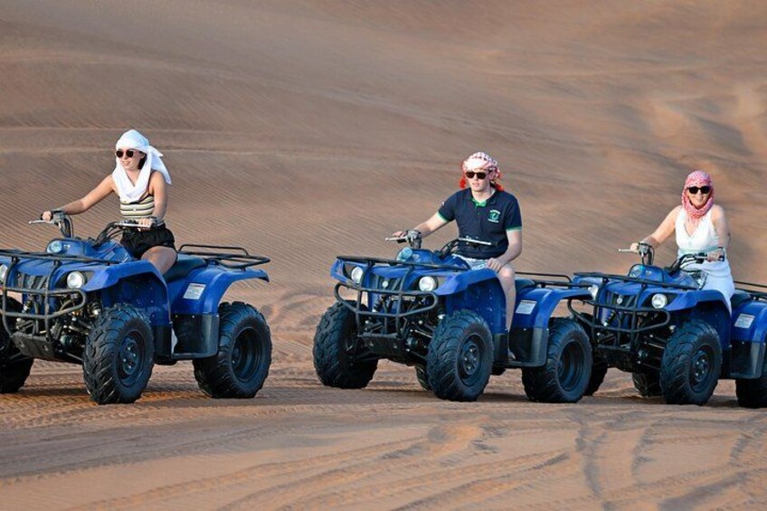 Tres personas montando cuatrimotos azules sobre terreno arenoso. 3