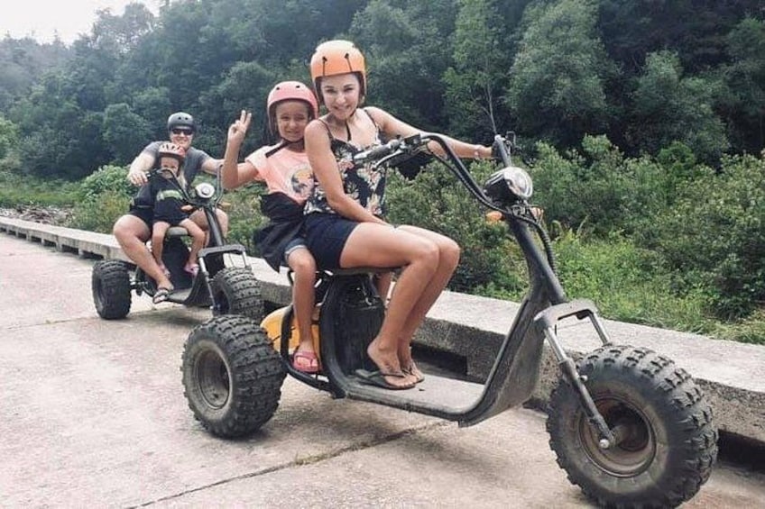 Tres personas en patinetes eléctricos sobre un camino pavimentado, con follaje al fondo. 1