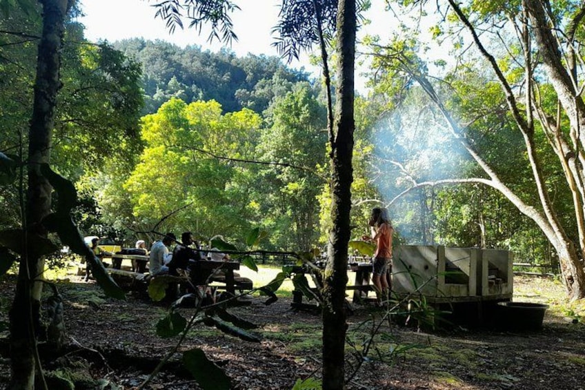 Zona boscosa con mesas de picnic y una persona de pie cerca de una construcción. 3