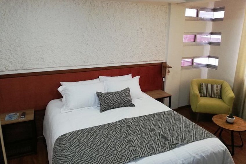 Una habitación de hotel con una cama, una mesita de noche, un sillón verde y una pequeña mesa con una lámpara. 4