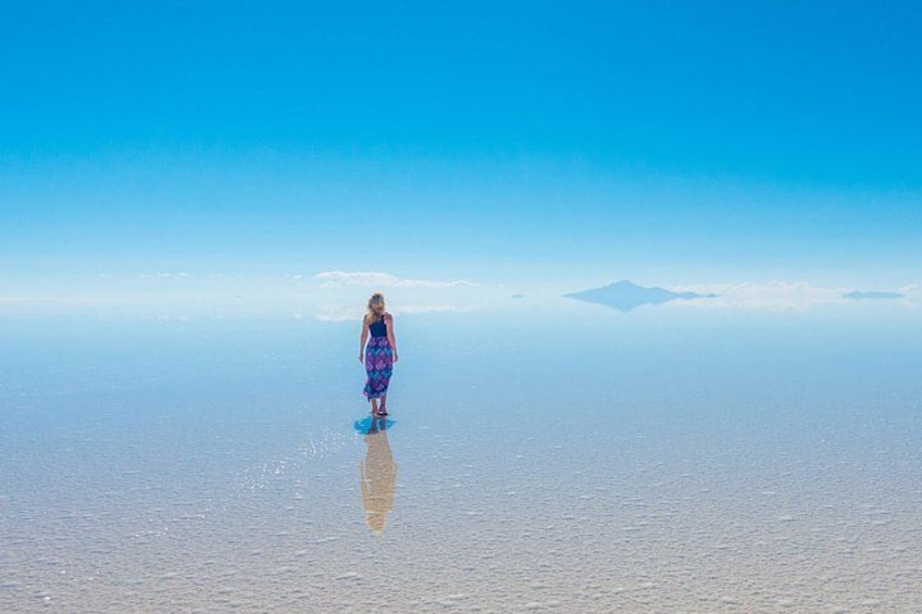 Una persona de pie sobre una superficie reflectante con una montaña al fondo. 1