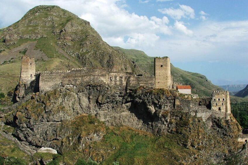 A medieval castle perched on a rocky hill with a red-roofed building and a tower. 4