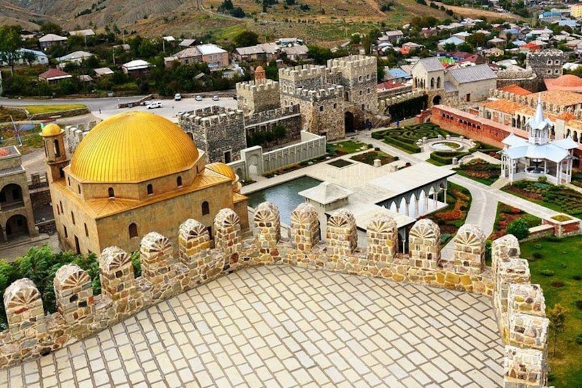 A historic cityscape with a prominent golden-domed building, a fortified castle, and a well-maintained public square. 4
