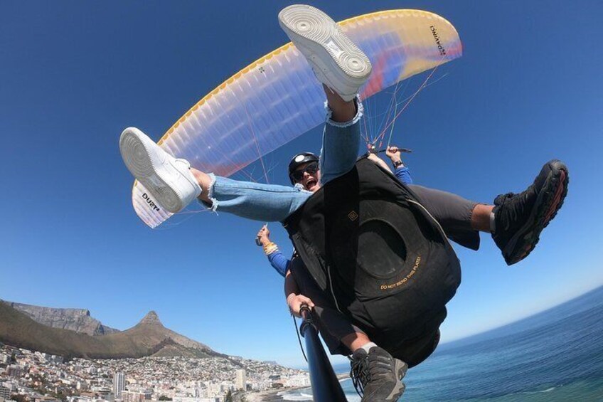 Una persona practicando parapente con un canopy colorido, sujetando un arnés, con un paisaje urbano y una montaña al fondo. 5