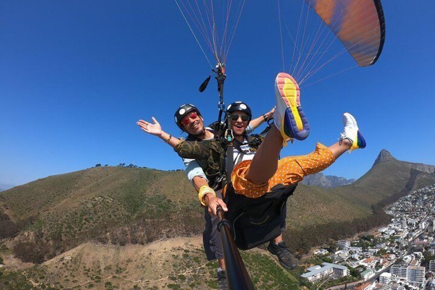 Dos personas hacen parapente con una ciudad y montañas al fondo. 3