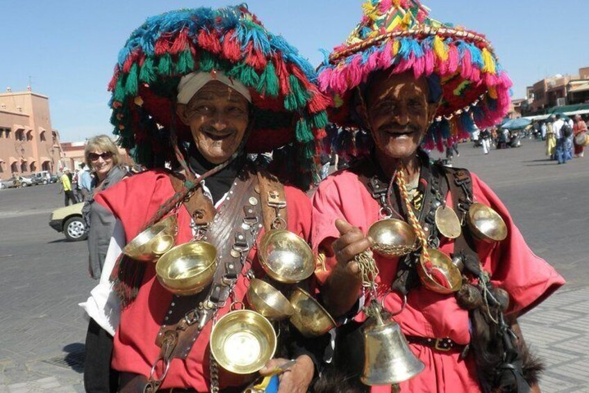 Two individuals in traditional attire with colorful headdresses and brass instruments. 1