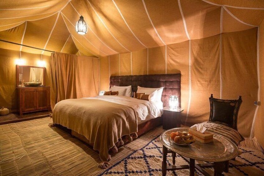 A tented room with a bed, a table with food, and a lamp. 3